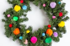 a Christmas wreath with colorful pompoms and a ribbon is a cool and fun decor idea for the holidays