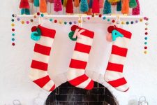 a bold Christmas mantel with colorful bottle brush trees, a colorful pompom garland, striped stockings with letters