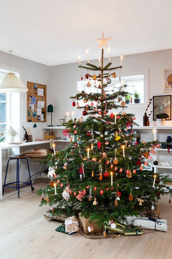 a bright Scandinavian Christmas tree with red ornaments, banners and garlands and some lights and faux candles