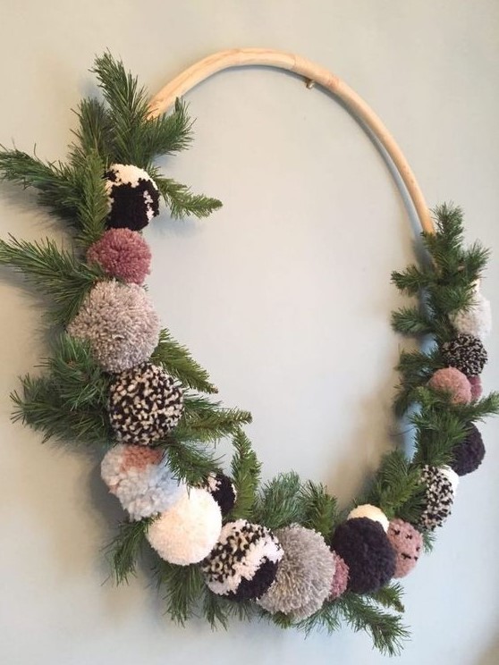 A cozy Christmas wreath of fir branches and pretty ombre and neutral colored pompoms is a lovely craft for the holidays