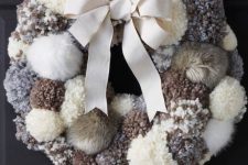 a cozy neutral pompom and faux fur wreath with a large bow is a very warming and cool decoration for your front door
