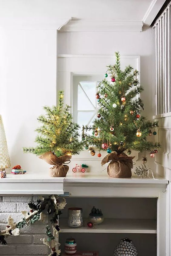 a duo of small Christmas trees wrapped in burlap and with lights and colorful ornaments is super cool