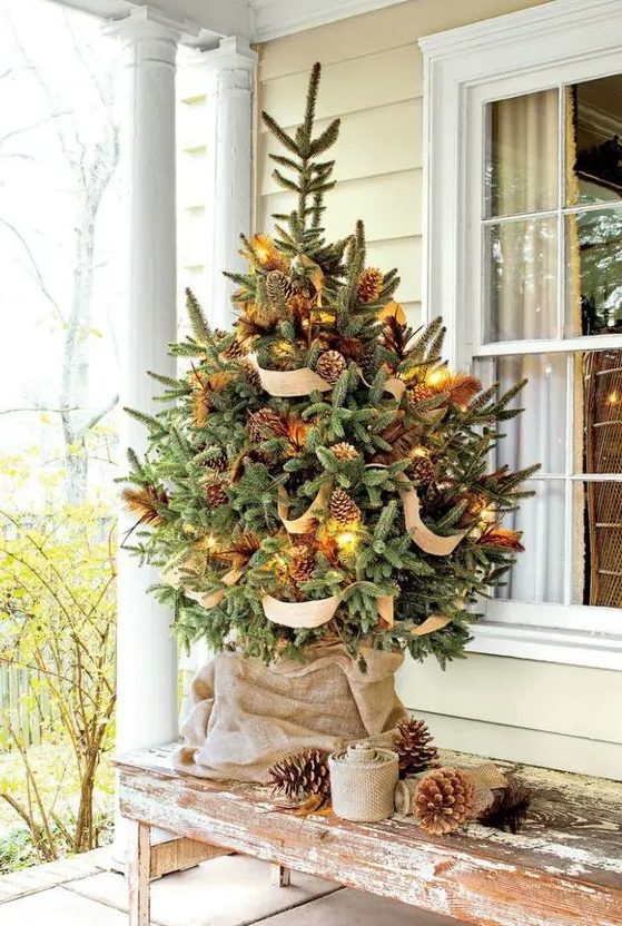 a gorgeous rustic Christmas tree styled with lights, pinecones, feathers and burlap looks amazing and will work for both indoors and outdoors