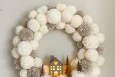 a grey and white pompom Christmas wreath with a lit up house and bottle brush trees is a cool decoration