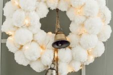 a heavenly beautiful white pompom Christmas wreath with lights and large bells is a cool winter or Christmas decor idea
