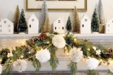 a lovely Christmas mantel with an evergreen and pinecone garland, a pompom one, lights, bottle brush trees and houses
