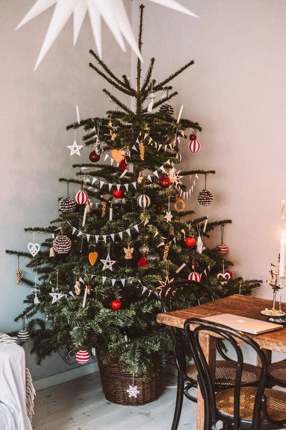 a lovely bright Scandinavian Christmas tree decorated with yellow and red ornaments, stripes, apples, faux candles and lights