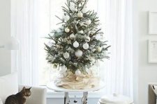 a modern snowy Christmas tree with lights, pinecones and white and gold ornaments looks beautiful and chic
