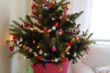 a potted Christmas tree decorated with colorful pompoms, ornaments and lights is a cool Christmas solution