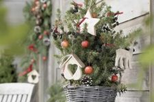 a small Christmas tree in a basket, with berries, pinecones, wooden ornaments is a super cool indoor and oiutdoor holiday decoration