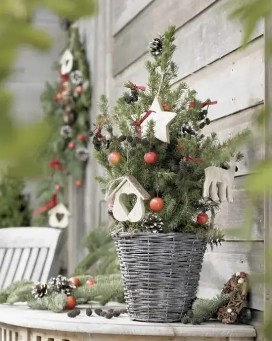 a small Christmas tree in a basket, with berries, pinecones, wooden ornaments is a super cool indoor and oiutdoor holiday decoration