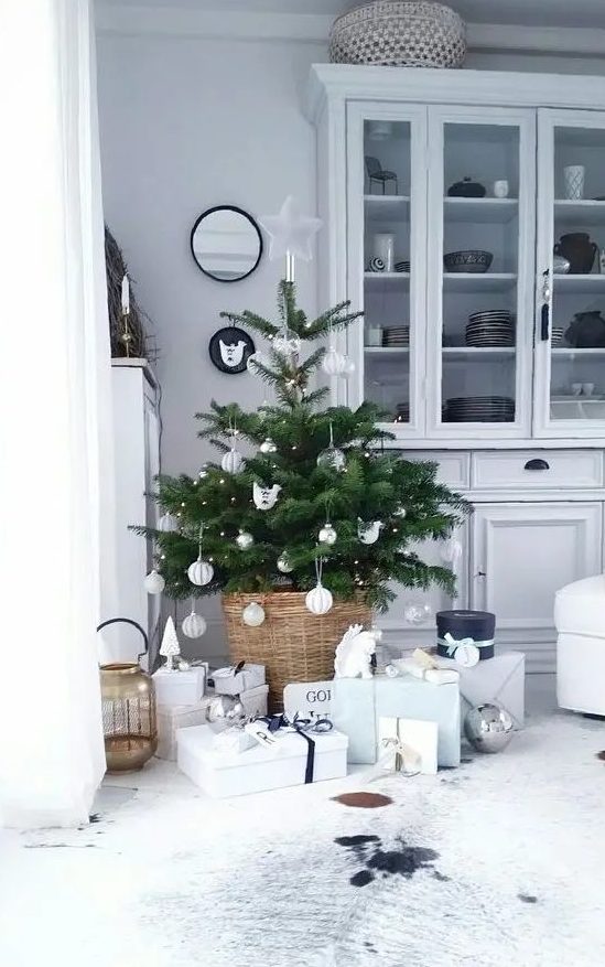 a small Nordic Christmas tree with lights and white and silver ornaments placed in a basjet and with neutral gift boxes under it is a chic idea for a modern space