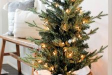 a stylish small Christmas tree decorated with lights and placed in a  basket is a cool idea for a rustic entryway