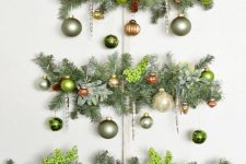a wall Christmas tree of evergreens, berries and muted green ornaments is a chic and catchy decoration