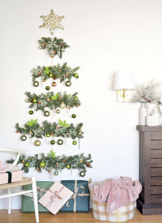 A wall mounted Christmas tree of evergreens, gold and green ornaments and a snowflake topper is cool