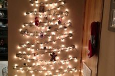 a wall-mounted Christmas tree of lights and with ornaments and decor is a cool and bold decor idea for the holidays