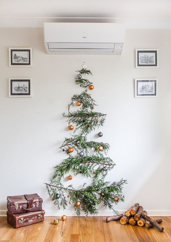 A wall mounted pine branch Christmas tree with gold and grey ornaments is a bold and catchy idea