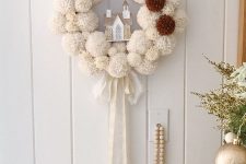 a white and brown pompom Christmas wreath with a ribbon bow and a house is a cool and cozy decor idea