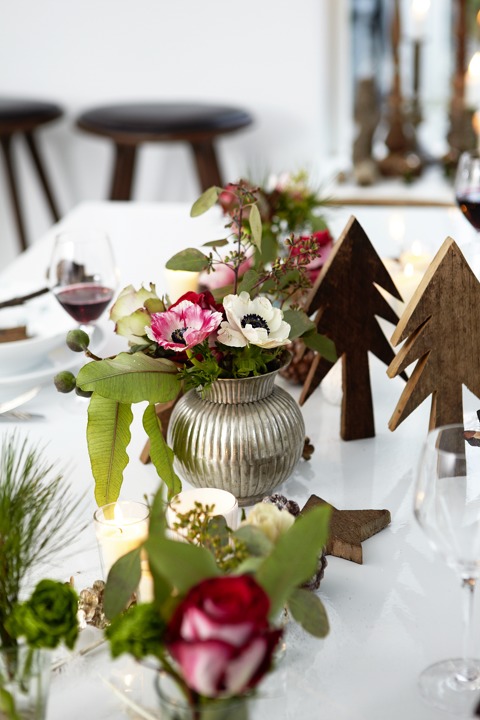 The table is decorated with wooden trees and floral centerpieces in traditional Christmas colors