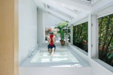 04 The bathtub is a large pool-like space clad with white tiles, with skylights and windows that show off greenery walls