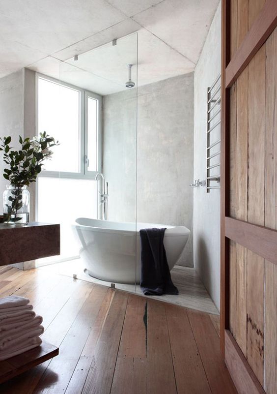 A modern rustic bathroom with a free standing sculptural bathtub and large yet frosty glass windows for natural light