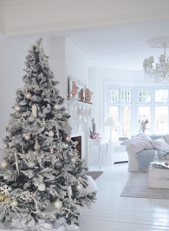 a snowy white and silver Christmas tree with various ornaments and white branch decorations
