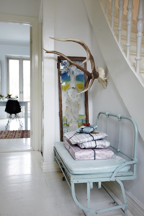 The entryway features a light blue beanch with a stack of gifts and antlers to use as a coat rack