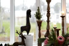 09 There’s a windowsill display with wooden candle holders, gifts, deer figurines and lush blooms and greenery in a vase