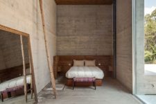 09 Wood panels and furniture add coziness to this industrial bedroom done with concrete, there’s a large mirror and a colorful footrest