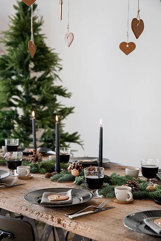 a hygge-inspired Christmas table setting with an evergreen garland, pinecones, nuts and black candles