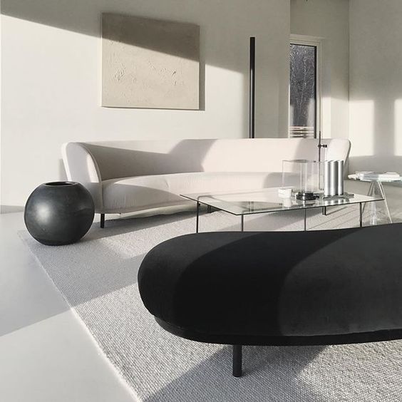 a minimal living room with black and white sofas, much natural light and glass coffee tables
