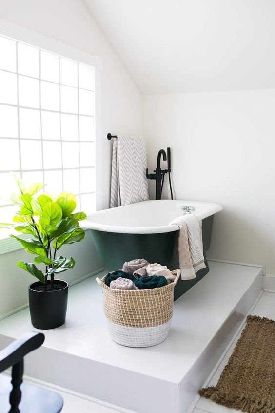 a platform bathing space with a black bathtub in the corner and a potted plant looks very cozy and comfy