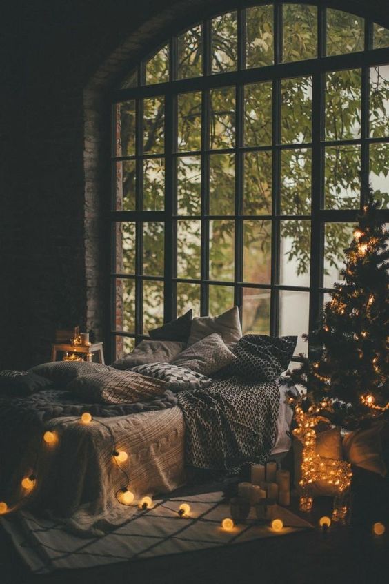 a bedroom lit up only with a Christmas tree with lights and a string of lights for more coziness