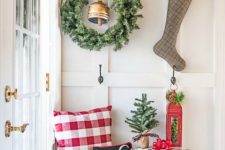 13 a large greenery wreath with a bell and a plaid stocking with evergreens and berries hanging on hooks