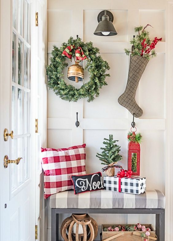 a large greenery wreath with a bell and a plaid stocking with evergreens and berries hanging on hooks