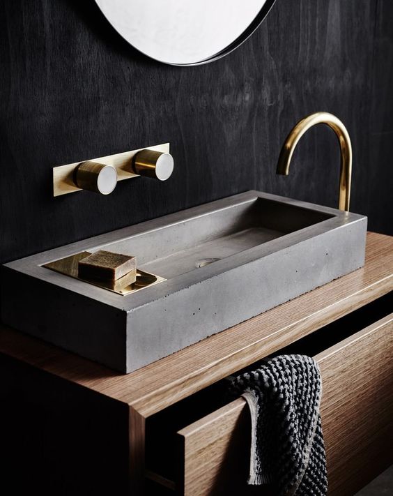 a sleek concrete geometric sink is accented with gold fixtures to give it a softer and chic look