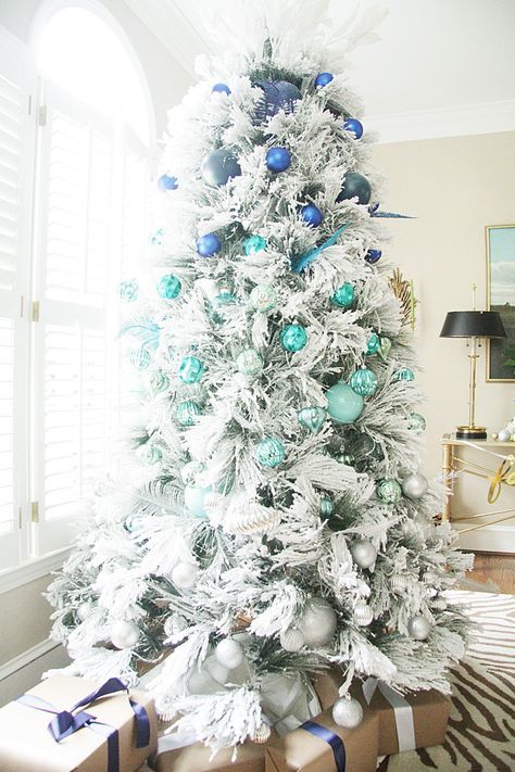a snowy Christmas tree decorated with ornaments from bright blue to turquoise and silver grey for an ombre effect