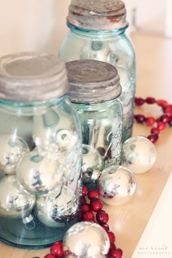 a wooden tray with mason jars filled with silver ornaments and a cranberry garland