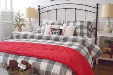 20 a farmhouse sleeping space with plaid, chunky knit, a trio of flocked Christmas arrangements over the bed and a display with pinecones and ornaments