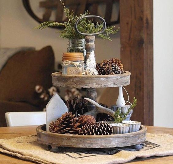 a two-tiered tray with pineccones, evergreens, candles and antlers for a woodland or natural feel