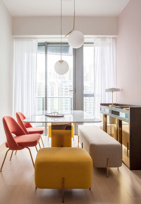 a duo of coral chairs, a yellow upholstered stool and a neutral upholstered bench make the space catchy
