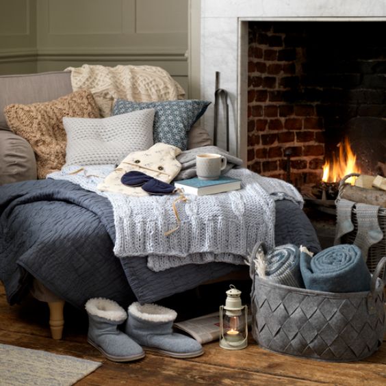 a super cozy nook with a large lounger with fabric and knit pillows, knit blankets and fabric throws