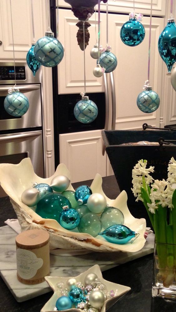 blue and turquoise Christmas ornaments hanging on a chandelier and in an oversized shell as a coastal display