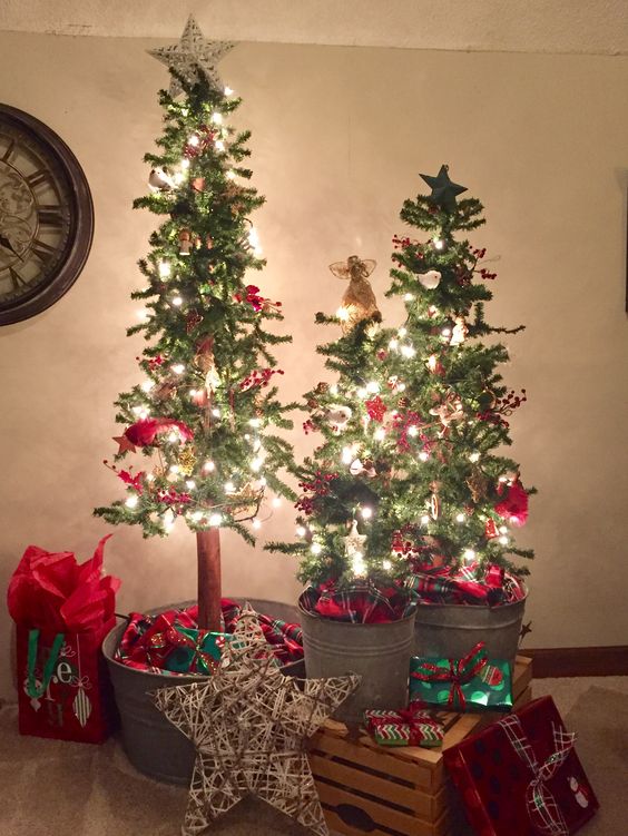 a trio of Christmas trees in galvanized buckets, with lights, red decor, stars and gifts all around