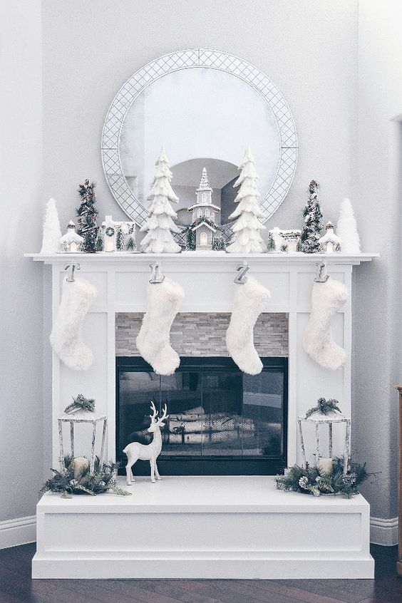 an all-white Christmas fireplace with stockings, lanterns, trees and snowy ornaments looks dreamy