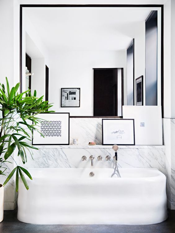 an oversized mirror over the bathtub and several artworks make the bathroom stylish and modern