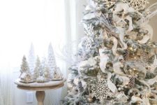 a flocked Christmas tree with lights, oversized snowflakes, pinecones, frozen branches and white ribbons looks like an outside one