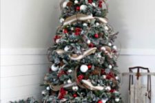 a rustic snowy Christmas tree done with white, silver and red ornaments, branches and striped burlap ribbon
