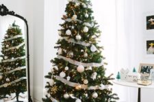 an elegant Christmas tree decorated with metallic ornaments, lights and black and white striped ribbons