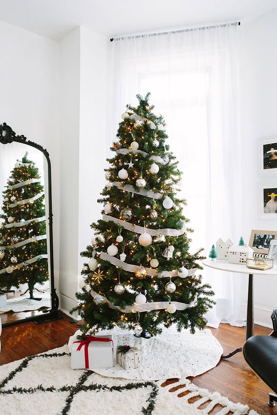 an elegant Christmas tree decorated with metallic ornaments, lights and black and white striped ribbons
